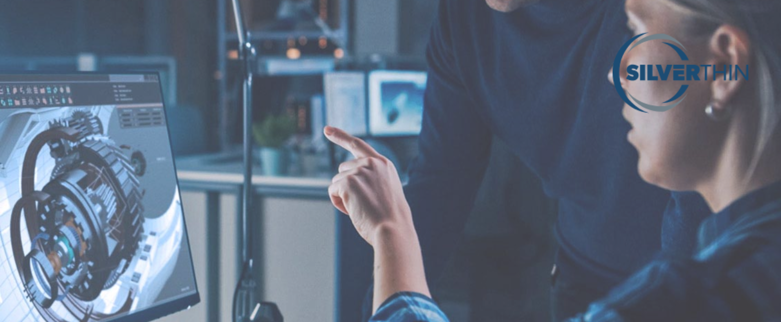 Two engineers review a detailed 3D rendering of a mechanical part on a computer screen in a modern Silverthin workshop.